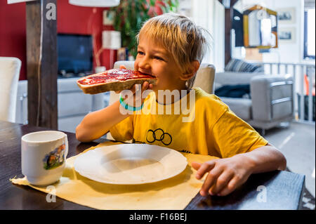 Blondschopf im gelben Trikot Essen an den Tisch Brot und Marmelade Stockfoto