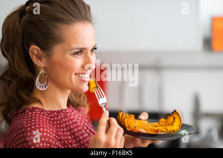 Eine Nahaufnahme Profil erschossen einer glücklich, elegante Frau als sie in die Ferne schaut, lächelt. Ihre Gabel ist bereit, bereit für sie, einen Bissen zu nehmen. Auf ihrem Teller gebratener Kürbis. Stockfoto