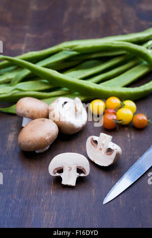 Pilze, Tomaten und Stangenbohnen auf einem Holzbrett. Stockfoto