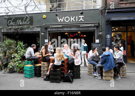 Junge Menschen Essen und Trinken sitzen auf Kisten außerhalb WOKIT Restaurant Mittags im Sommer in der Nähe von Borough Market in South London UK KATHY DEWITT Stockfoto