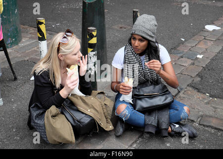 Zwei Freundinnen sitzen zusammen und reden und essen Wraps auf dem Borough Market in Southwark, South London UK KATHY DEWITT Stockfoto