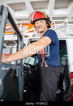 Lächelnde Feuerwehrmann stehend auf LKW Stockfoto