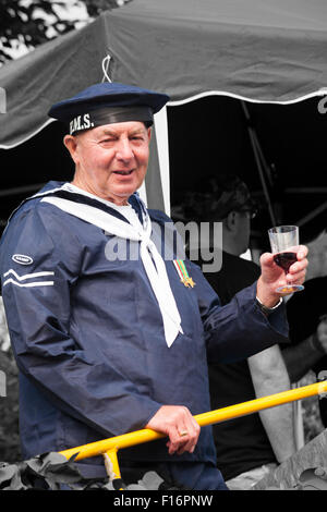 Mann in HMS US Navy Kostüm halten Glas Rotwein bei Swanage Karnevalsumzug im Juli mit dem Thema der Superhelden Stockfoto