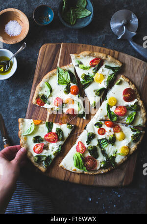 Padron Pfeffer und Cherry Tomaten Pizza, glutenfrei und Vollkornprodukte. Eine Hand, ein Stück nehmen. Stockfoto