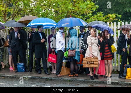 Junge Oper Fans warten im strömenden Regen bei Lewes Bahnhof einen Bus nehmen sie in Glyndebourne Opera House, Lewes, Sussex, UK Stockfoto