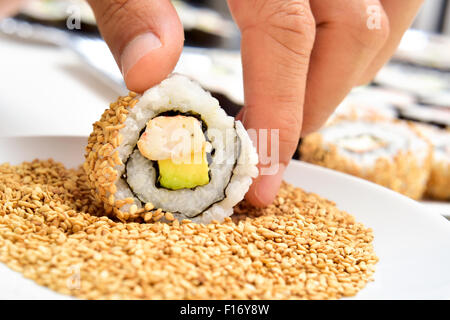 Nahaufnahme eines jungen Mannes Vorbereitung Uramaki, gefüllt mit Avocado und Garnelen und garniert mit Sesam Stockfoto