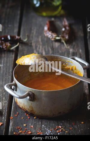 Aluminium-Pfanne mit Resten der Creme von Möhrensuppe mit red hot Chili peppers. Über alten Holztisch mit Vintage Löffel und trockenen peppe Stockfoto