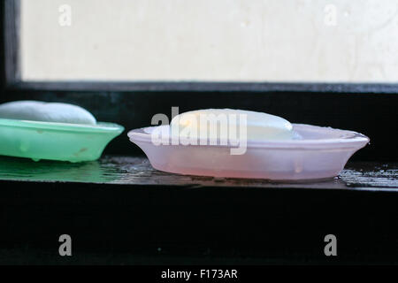 Zwei Stäbe von Glycerin Seife sitzen in zwei separaten Seifenschalen, rosa und grün auf der Fensterbank Stockfoto