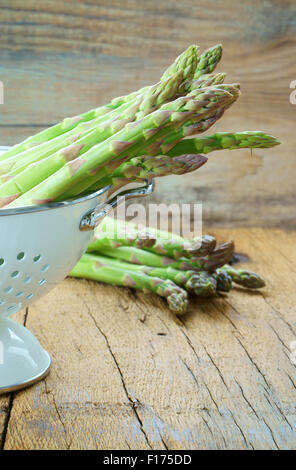 Frischer grüner Spargel in einem weißen Sieb auf einem rustikalen Holztisch Stockfoto