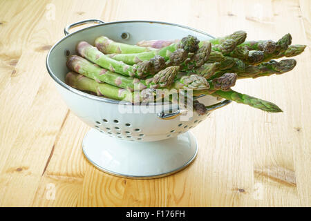 Frischer grüner Spargel in einem weißen Emaille Sieb auf einem rustikalen Holztisch Stockfoto