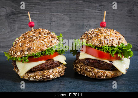 Zwei Gourmet-Hamburger mit Käse und frischem Gemüse auf Mehrkorn Brötchen auf dunklem Hintergrund Stockfoto