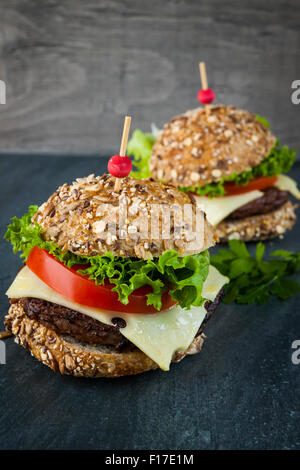 Zwei Gourmet-Hamburger mit Käse und frischem Gemüse auf Mehrkorn Brötchen auf dunklem Hintergrund Stockfoto