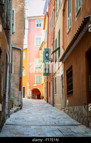 Schmale gepflasterte Straße mit hellen Gebäuden in der mittelalterlichen Stadt Villefranche-Sur-Mer an der Côte d ' Azur, Frankreich. Stockfoto