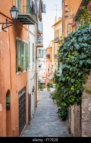 Schmale gepflasterte Straße mit hellen Gebäuden und grünen Efeu zum Mittelmeer in der mittelalterlichen Stadt Villefranche-Sur-Mer Stockfoto