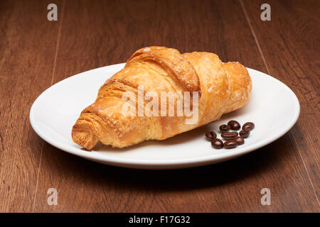 Frische französische Croissant und Kaffee Bohnen auf weißen Keramikplatte auf dunklen Holztisch Hintergrund Stockfoto