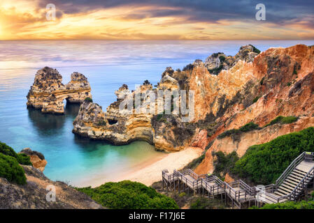 Der schöne Strand von Camilo in Lagos, Portugal, mit seinen herrlichen Klippen und den blauen Ozean bunt beleuchtet bei Sonnenaufgang Stockfoto