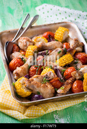 Gebratenes Huhn mit Gemüse in Metall Backblech. Hähnchenflügel, Tomaten, Mais und Zwiebeln. Grüner Hintergrund, selektiven Fokus Stockfoto