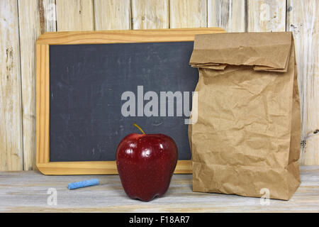 Braunem Papier Tasche und roten Apfel mit schwarzen Tafel auf Tünche Holz. Stockfoto