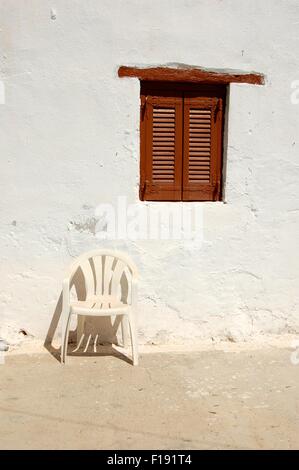 Fensterläden, Fenster und weißen Plastikstuhl gegen eine weiße Wand in Loutro Kreta Griechenland Stockfoto