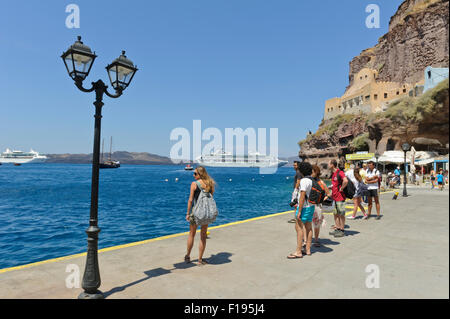 Touristen in Sommerkleidung stehend auf dem Kai von Santorini alten Hafen mit zwei Kreuzfahrtschiffe in der Ferne, Griechenland. Stockfoto