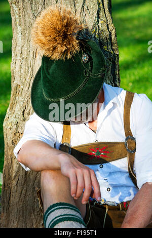 Mann in bayerischer Tracht sitzen durch einen Baum und schläft Stockfoto