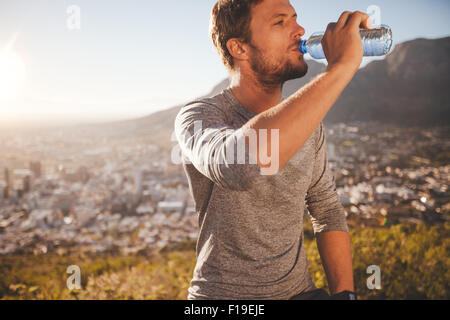 Junge Läufer eine Pause nach dem Morgenlauf Trinkwasser. Junger Mann entspannen nach einem laufenden Trainingseinheit im Freien in co Stockfoto