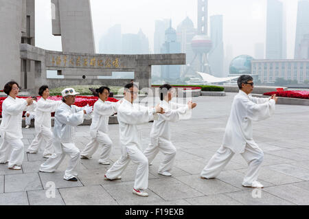 Tai Chi Gruppe in passender Ausrüstung Übungen in der Nähe von Shanghai Bund im Hinblick auf die Skyline von Pudong, die im Smog verdeckt wird. Stockfoto