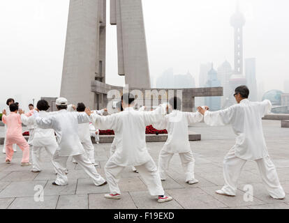 Tai Chi Gruppe in passender Ausrüstung Übungen in der Nähe von Shanghai Bund im Hinblick auf die Skyline von Pudong, die im Smog verdeckt wird. Stockfoto