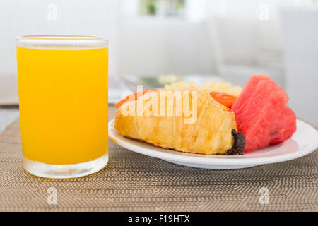 Frühstück mit Orangensaft, Croissants und Obst am Esstisch Stockfoto