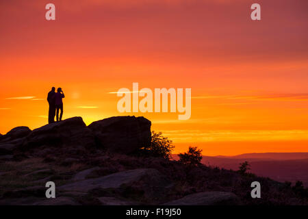 Paar steht auf Felsen mit Blick auf Golden orange Sonnenuntergang Chevin, Otley, West Yorkshire Stockfoto