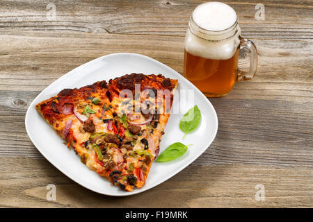 Zwei Scheiben frisch gebackene Pizza in einem weißen Teller mit einem Pint Recht gezapftes Bier-Einstellung auf einem rustikalen Holztisch. Stockfoto