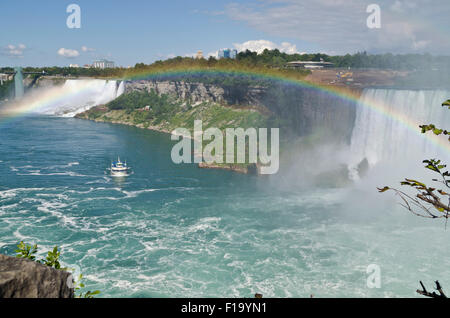 Blick auf die American Falls und Horseshoe Falls von kanadischen Seite von Niagara Falls. Regenbogen über dem Wasser.  Magd des Bootes Nebel. Stockfoto