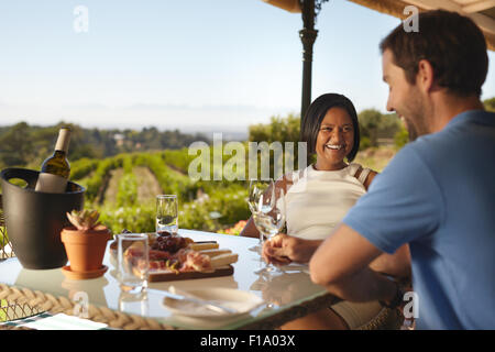 Glückliches junges Paar im Weingut Restaurant mit Weinberg im Hintergrund. Lächelnde junge Frau mit einem Mann am Tisch trinken wi Stockfoto