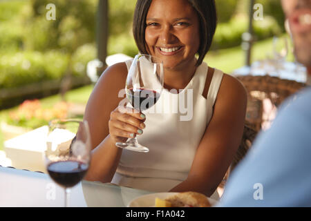 Porträt von schöne junge Frau sitzt an einem Tisch im Weingut hält ein Glas Rotwein und lächelt in die Kamera. Stockfoto