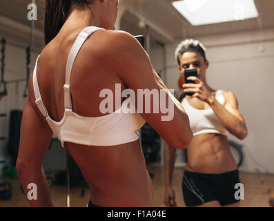 Sportliche junge Frau, die ein Bild von sich selbst in einem Spiegel. Fitness-Modell, wobei eine Selfie vor einem Spiegel im Fitness-Studio. Stockfoto
