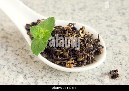 Elite chinesische getrocknete schwarzer Tee mit Minze auf Löffel über rustikale Stein Hintergrund hautnah Stockfoto
