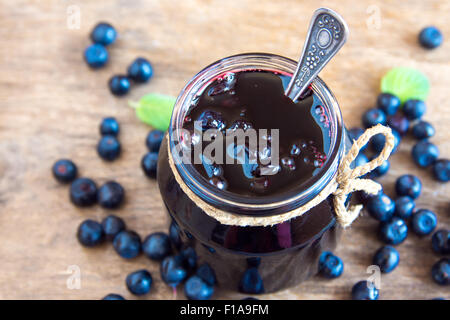 Blaubeeren Marmelade im Glas mit Beeren und Blätter über rustikalen Holztisch Stockfoto