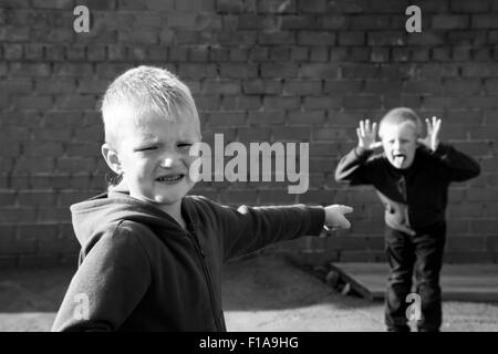 Kinder Streit und Hänseleien zwischen zwei Jungs (Brüder, Freunde) im Freien in der Nähe von roten Backsteinmauer Stockfoto