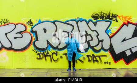 London, UK.  31. August 2015.  Ein Mann in einem Poncho macht einen Anruf auf seinem Handy vor dem Hintergrund eines Shops mit Brettern vernagelt am zweiten Tag der Notting Hill Carnival im Westen von London. Bildnachweis: Stephen Chung / Alamy Live News Stockfoto