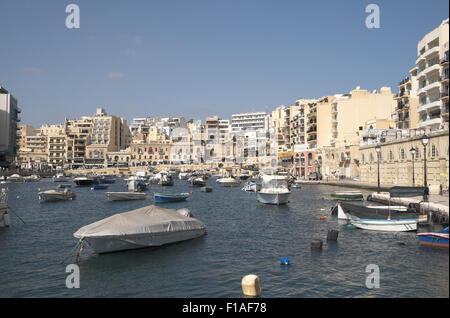 Hell traditionelle Fischerboote mit steinernen Gebäuden jenseits, St Julian's Bay, Malta gemalt. Stockfoto