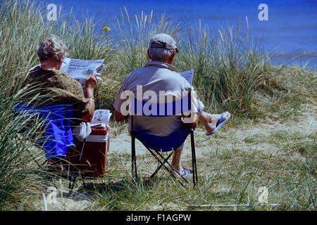 Ältere Paare sitzen auf einem Strand lesen. England. Großbritannien Stockfoto