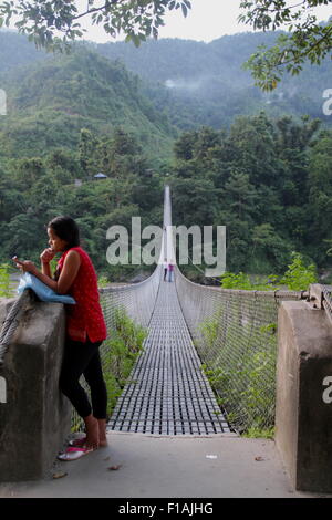 Junge Frau auf ihrem Handy einen Freund th Ende der Fußgängerbrücke überqueren Trishuli Flusses in Kurintar, Napal wartete Stockfoto