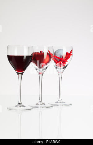 Weingläser mit roten Wein, Herz und Golf Ball auf weißen Tisch Stockfoto