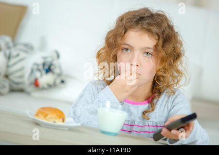 Kleines Mädchen vor dem Fernseher wie sie ihr Frühstück hat Stockfoto