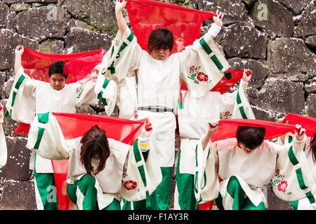 Japanische Yosakoi dance Team. Die Tänzer tragen weiße und grüne Kostümen tanzen während wirbelnden roten Tücher. Schloss Stein Wand Hintergrund. Stockfoto