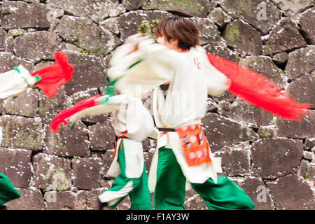 Japanische Yosakoi dance Team. Die Tänzer tragen weiße und grüne Kostümen tanzen während wirbelnden roten Tücher. Schloss Stein Wand Hintergrund. Stockfoto