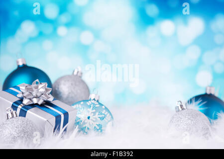 Blau und Silber Weihnachtskugeln und ein Geschenk auf eine weiche federleichte Oberfläche vor defokussierten blaue und weiße Lichter. Stockfoto