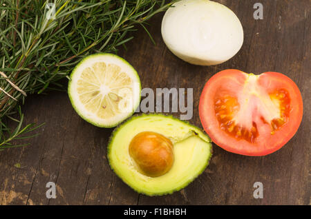 Reife aromatische Rosmarin, Kalk, Zwiebeln, Avocado und Tomaten schneiden Sie in Hälften auf Holzbrett Stockfoto