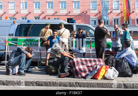 München, Deutschland. 1. Sep, 2015. Einige Flüchtlinge sitzen auf dem Boden, einige zeigen einer Geste des Friedens während der Wartezeit für den Transport eines Flüchtlings Aufnahmezentren, am Münchner Hauptbahnhof, in München, 1. September 2015. Foto: NICOLAS ARMER/Dpa/Alamy Live News Stockfoto