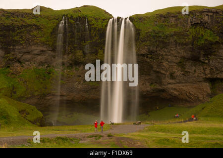 Langzeitaufnahme des Seljalandsfoss Wasserfalls mit verschwommenem Wasser und Touristen, die an seiner Basis stehen - ein berühmtes Wahrzeichen an der Südküste Islands Stockfoto